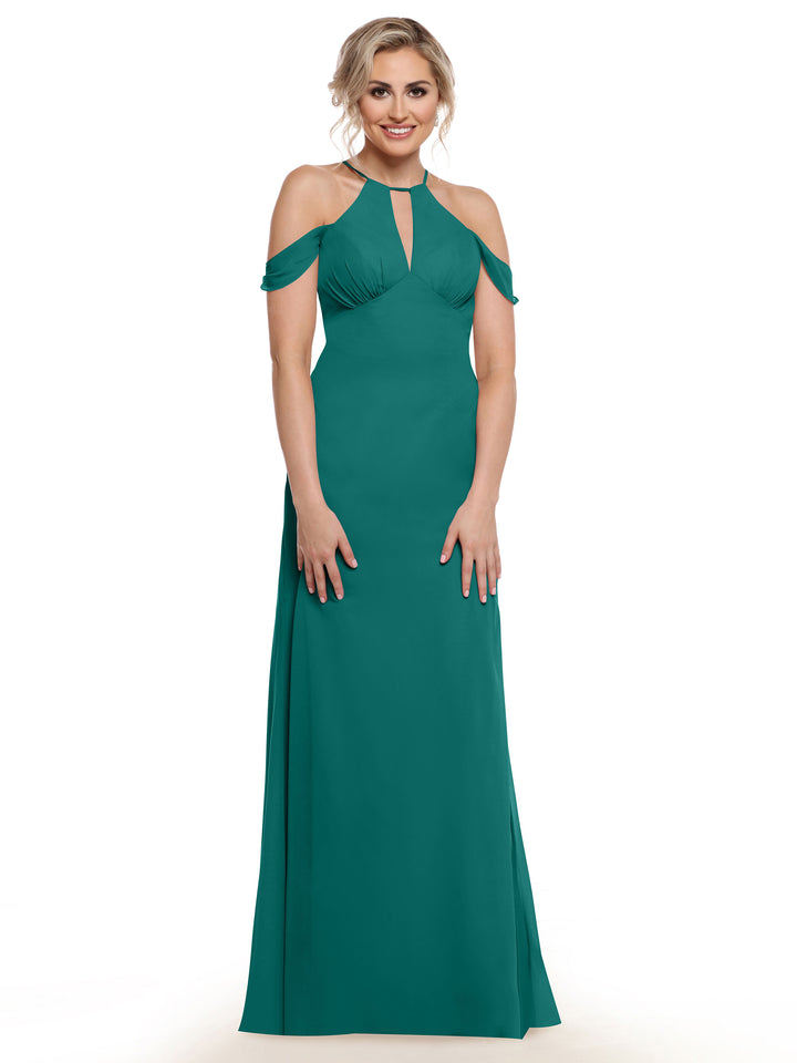 A woman with blonde hair in an updo wears Avery Austin’s floor-length teal dress (Style 80148) featuring chiffon cap sleeves and a keyhole neckline, standing and smiling against a white background.
