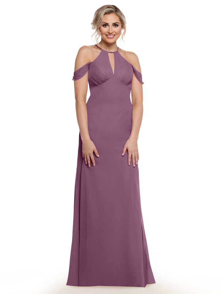 A woman stands smiling against a white background in Avery Austin’s 80148, a mauve purple floor-length gown with chiffon cap sleeves and a front keyhole cutout.