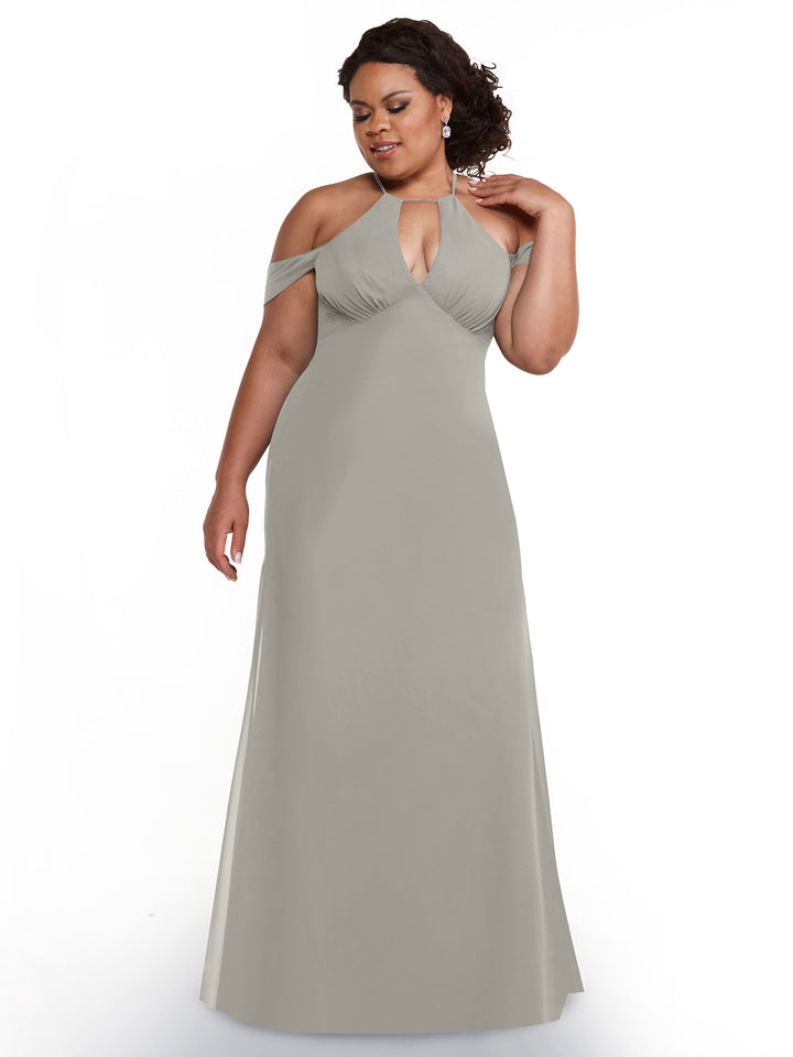 A woman models Avery Austin’s floor-length, light gray off-the-shoulder dress (style 80148) with chiffon cap sleeves and a keyhole neckline, standing against a white background while gently touching her neck and looking downward.