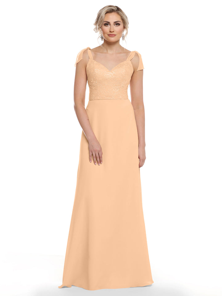 A woman models Avery Austin’s 80149—a long peach chiffon dress with floral lace bodice, sheer cap sleeves, and flowing skirt—standing against a plain white background.