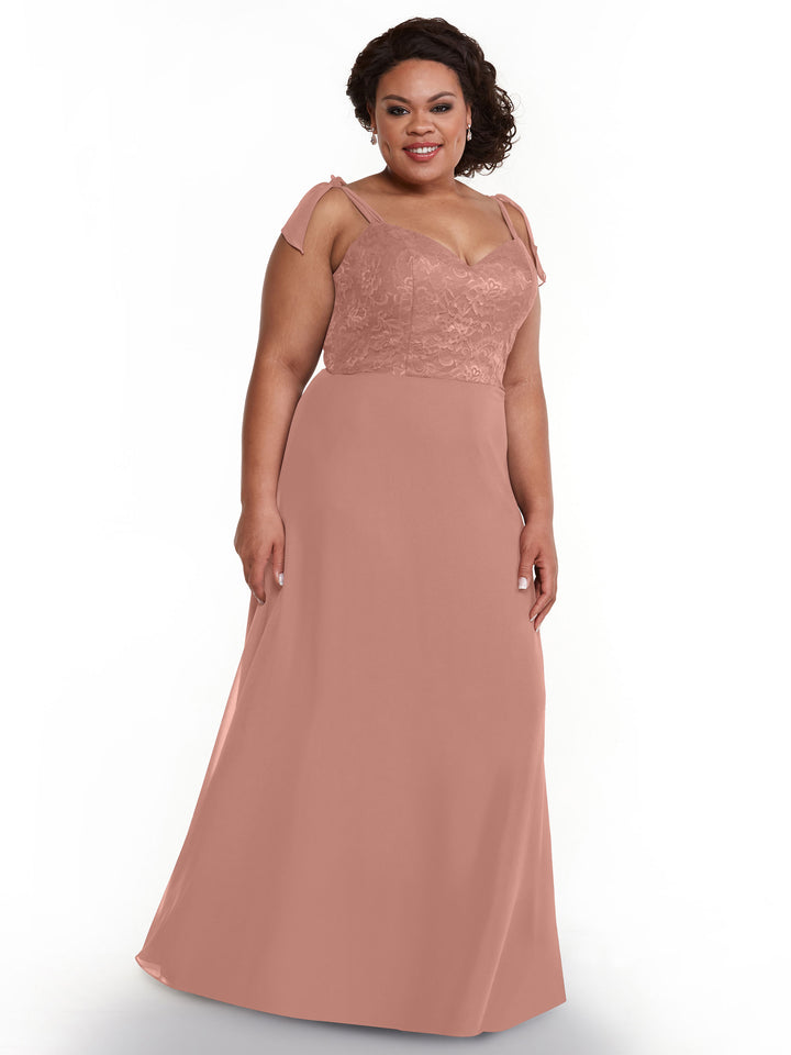 A woman wears Avery Austin style 80149, a long dusty rose pink chiffon dress with floral lace bodice and sheer cap sleeves, smiling against a plain white background.