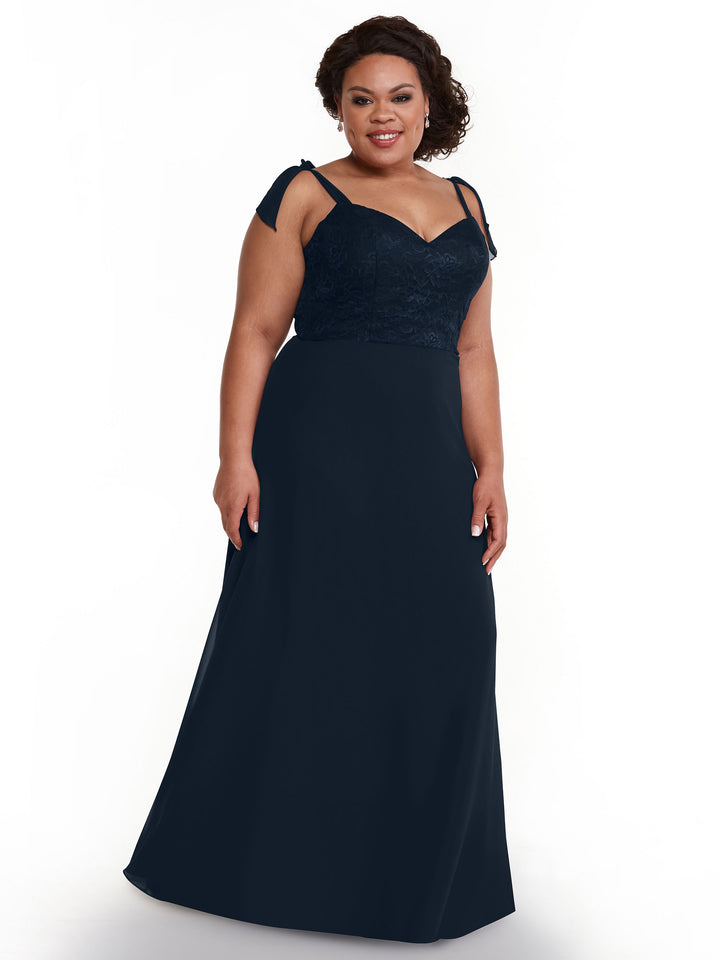 A woman in the Avery Austin 80149 dress, a floor-length navy chiffon gown with a floral lace bodice and self-tie straps, smiles against a plain white background.