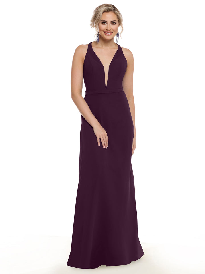 A woman with light hair styled up and statement earrings smiles against a plain white background, wearing Avery Austin’s 80150 dress in deep purple with a plunging neckline.