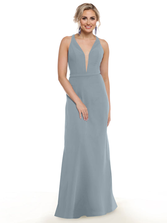 A woman stands smiling in the Avery Austin 80150, a sleeveless, floor-length gown with a deep V-neckline. Her light hair is styled up and she wears dangling earrings, posing against a plain white background.