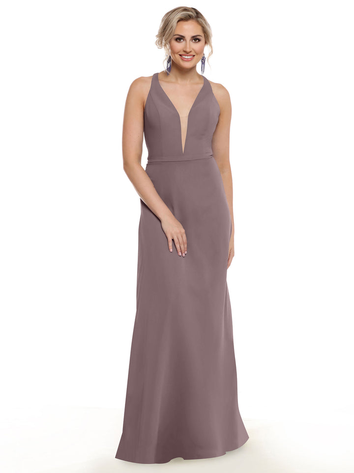 A woman stands and smiles against a white background, wearing Avery Austin’s 80150—an electrifying sleeveless mauve gown featuring a deep V neckline and geometric cut-outs. Her light hair is styled up, and she pairs the look with dangling earrings.