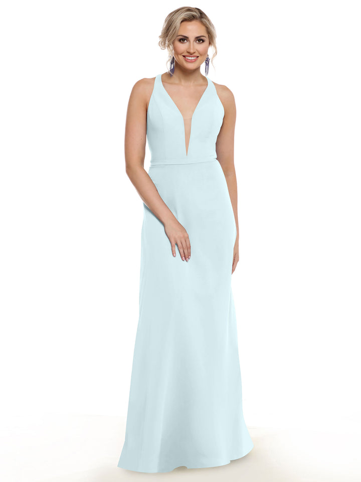 A woman stands and smiles against a white background, wearing Avery Austin’s electrifying light blue floor-length gown, style 80150, featuring a plunging neckline.