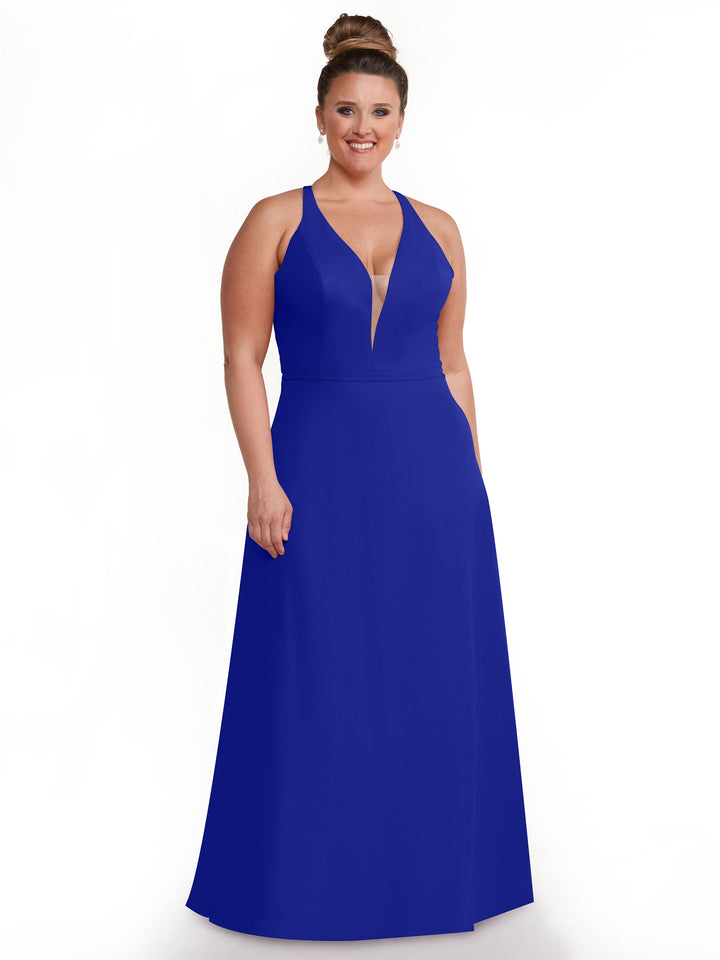 A woman with light skin and brown hair in a bun wears Avery Austin’s royal blue, sleeveless floor-length gown (Style 80150) with a deep V-neckline. She smiles while standing against a plain white background.
