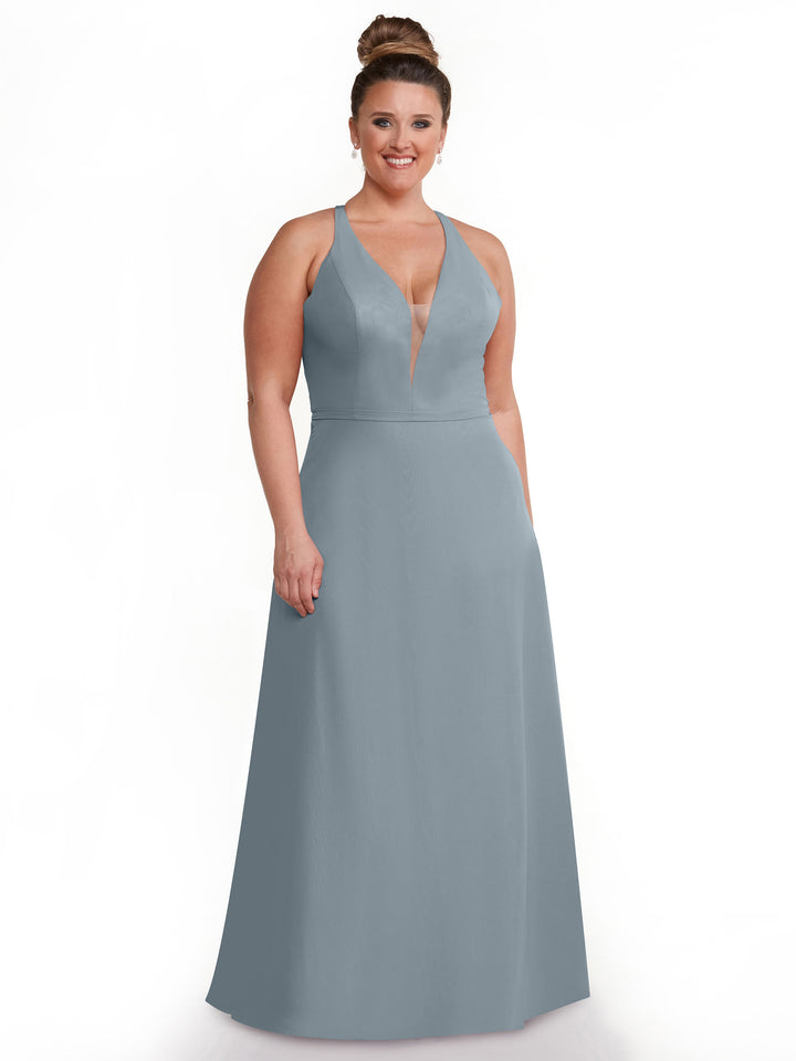 A woman with light skin and brown hair in a bun models Avery Austin’s 80150, a sleeveless light blue-grey gown with a plunging neckline and floor-length A-line skirt, standing against a white background.