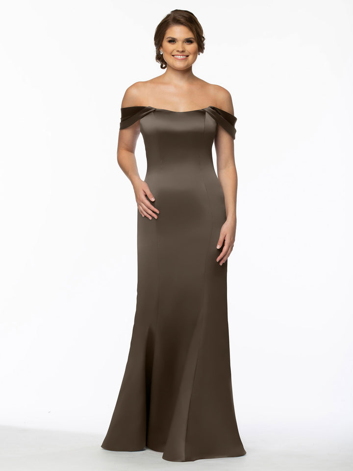 A woman smiles in the Avery Austin 80151, a fitted, off-the-shoulder brown gown with a slight mermaid silhouette. The floor-length dress flatters her figure as she poses gracefully against a plain white background.