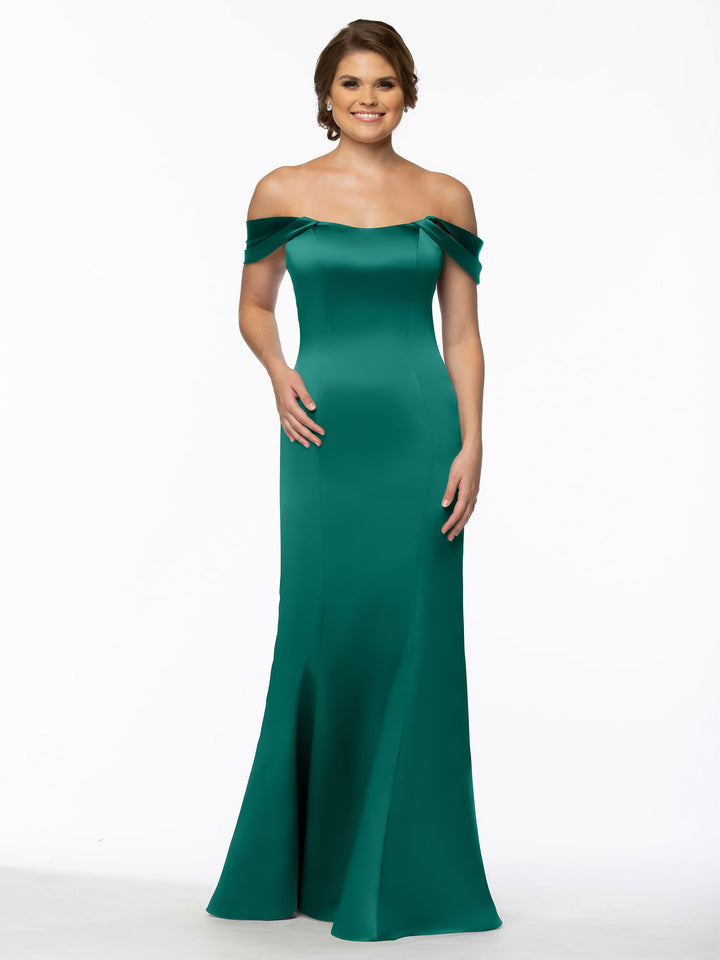 A woman smiles in Avery Austin’s 80151, a fitted off-the-shoulder emerald gown with a flared hem, standing out vividly against the plain white background.