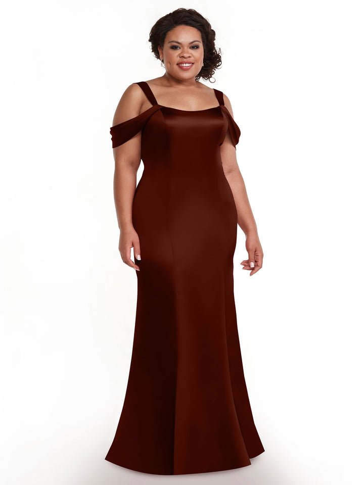 A woman stands smiling against a white background in the Avery Austin 80151 gown—a floor-length, off-the-shoulder dress with thin convertible straps and a fitted silhouette. The dark burgundy design radiates timeless sophistication.