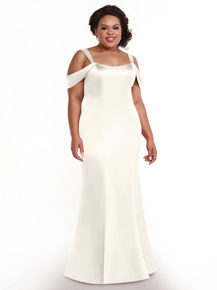 A woman stands smiling against a plain white background, wearing the Avery Austin 80151 dress—an elegant, off-the-shoulder style with thin straps and a fitted silhouette.