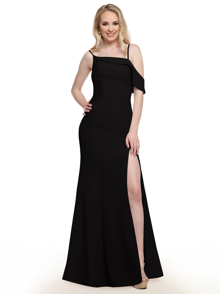 A woman with long blonde hair wears Avery Austin’s 80153 black fit-and-flare bridesmaid dress, featuring an asymmetrical neckline and high slit, as she stands and smiles against a white background.
