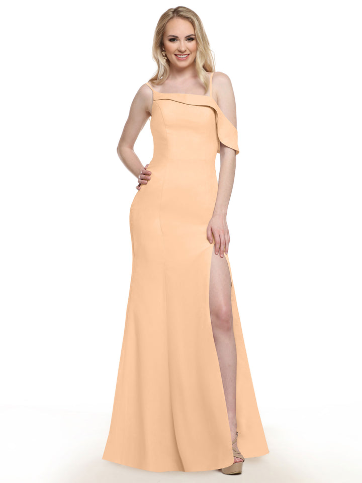 A woman stands smiling against a white background, wearing Avery Austin style 80153—a peach chiffon bridesmaid dress with a one-shoulder neckline and thigh-high slit—one hand on her hip, the other relaxed by her side.