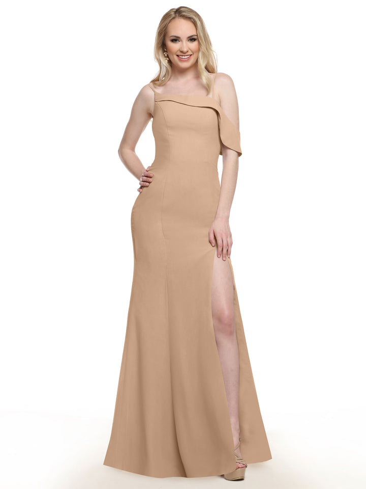 A woman poses, smiling with one hand on her hip and the other by her side, wearing Avery Austin’s TH-80153 bridesmaid dress in Buff—a long, one-sleeve design with a high slit—against a white background.