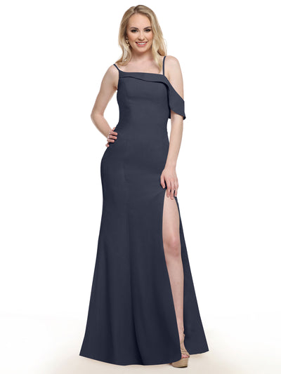A woman wears the Avery Austin 80153 indigo floor-length dress with a high slit, asymmetrical neckline, and ruffle sleeve, smiling with one hand on her hip against a white background.