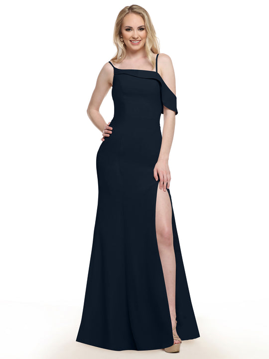 A woman with long blonde hair smiles in the Avery Austin 80153 dark navy one-sleeve bridesmaid dress with a high slit, nude heels, and one hand on her hip against a plain white background.