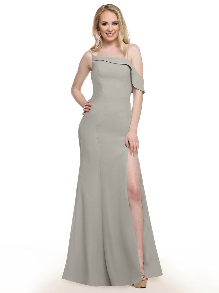 A woman in the Avery Austin 80153, a light gray chiffon floor-length bridesmaid dress with an asymmetric neckline and high slit, poses and smiles against a plain white background.