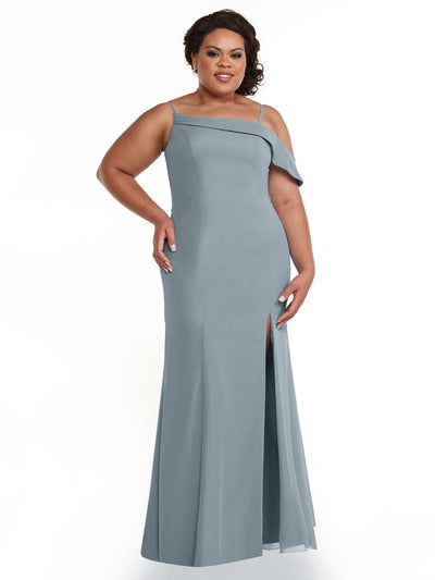 A woman poses smiling with her hand on her hip against a white background, wearing Avery Austin style 80153—a floor-length, dusty blue one-shoulder evening gown with an asymmetrical ruffle sleeve and thigh-high slit.