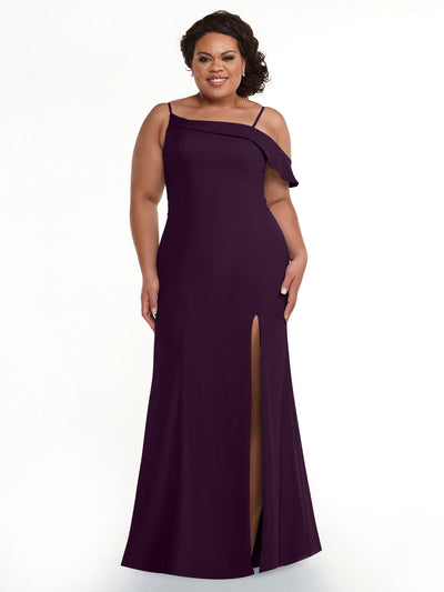 A woman stands and smiles against a white background wearing Avery Austin's 80153 floor-length eggplant dress featuring a high slit and asymmetrical ruffle sleeve.