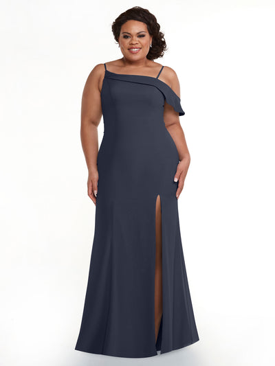 A woman in an Indigo Avery Austin 80153 floor-length dress with an asymmetrical ruffle sleeve and thigh-high slit stands smiling against a plain white background.