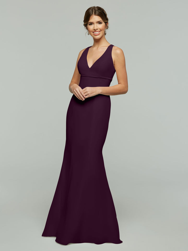 A woman smiles in the Avery Austin 80155, a sleeveless, floor-length aubergine chiffon dress with a V-neckline and open keyhole back, set against a plain light gray background.