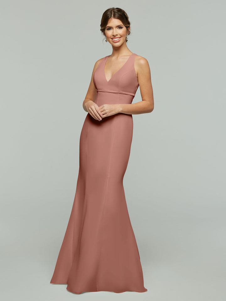 A woman smiles in the Avery Austin 80155, a sleeveless floor-length rose chiffon fit and flare dress with a V-neckline, set against a plain light gray background.
