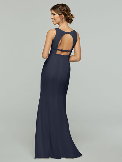 A woman faces away, looking to the side, modeling Avery Austin’s floor-length sleeveless navy chiffon dress (style 80155) with a keyhole back and decorative straps, set against a plain light gray background.