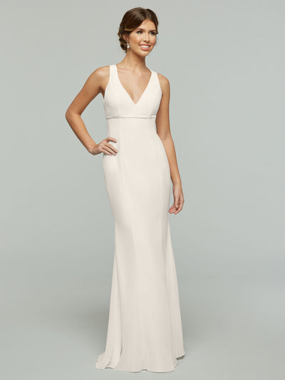 A woman poses in the Avery Austin 80155, a sleeveless chiffon gown with a V-neckline and fitted waist, smiling with one hand on her hip against a plain light gray background.