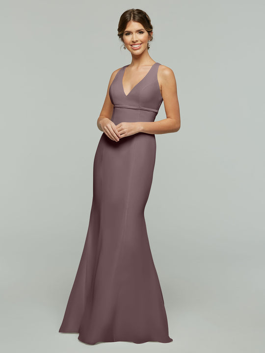 A woman smiles in Avery Austin's 80155, a fit and flare mauve chiffon dress featuring a sleeveless design, deep V-neckline, and open keyhole back, set against a plain light gray background.