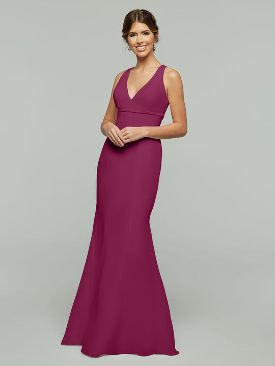 A woman wearing the Avery Austin 80155—a sleeveless, floor-length magenta chiffon dress with a V-neckline and fit and flare silhouette—stands smiling against a plain light gray background.