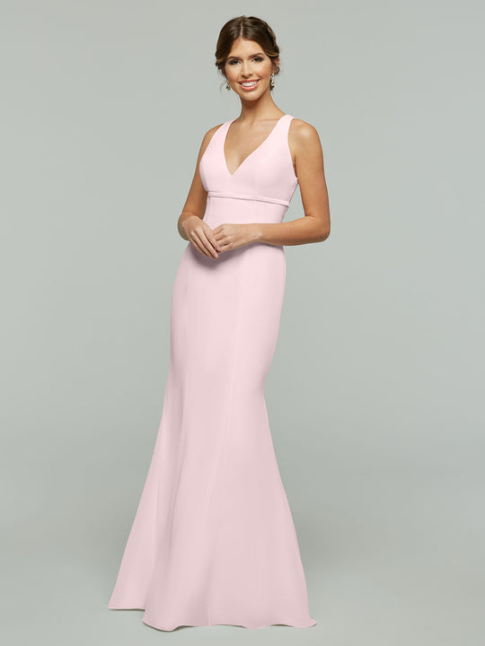A woman in the Avery Austin TH-80155 Rose Petal dress, a sleeveless, floor-length chiffon gown with a V-neckline and open back, smiles against a plain gray background.