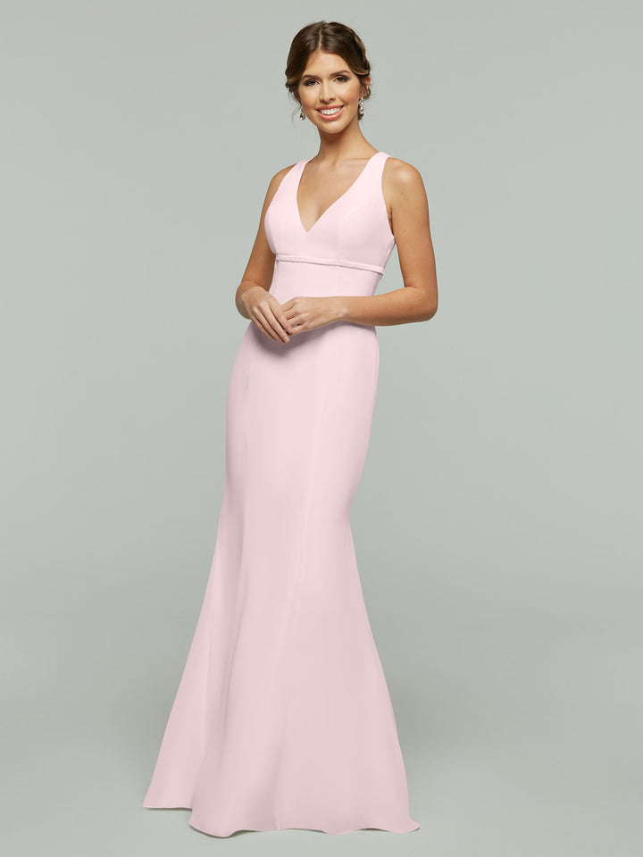 A woman in the Avery Austin TH-80155 Rose Petal dress, a sleeveless, floor-length chiffon gown with a V-neckline and open back, smiles against a plain gray background.
