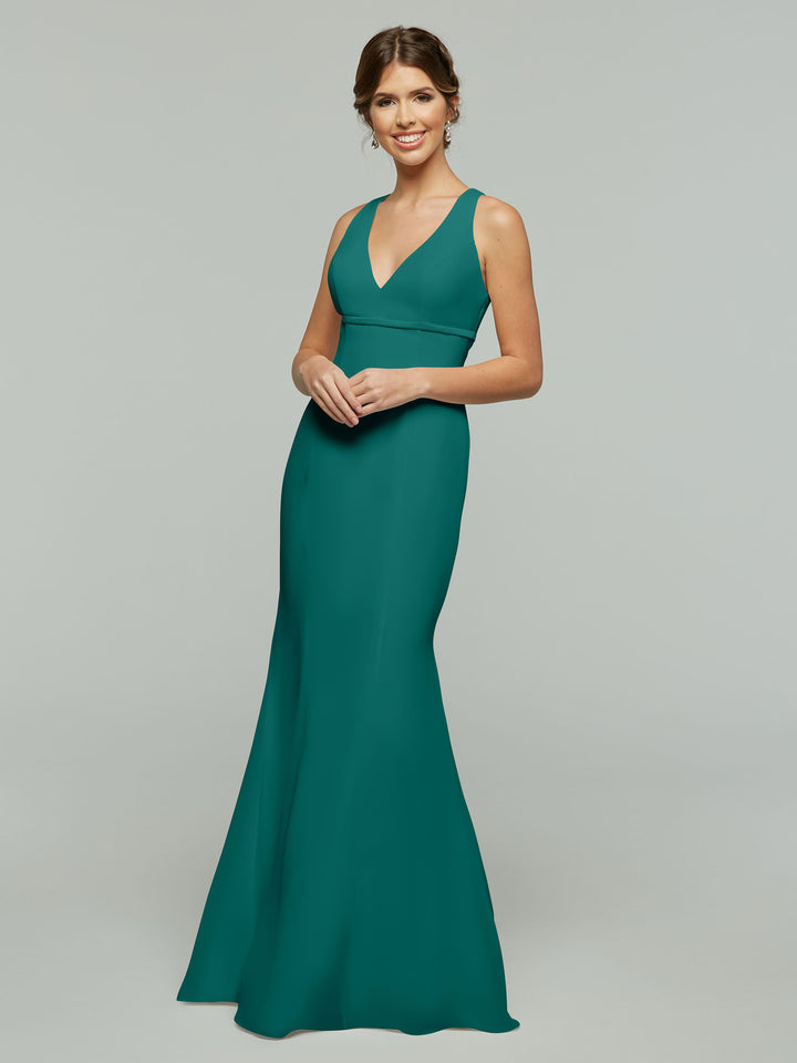 A woman smiles in Avery Austin’s 80155: a sleeveless, floor-length teal chiffon dress with a V-neckline and keyhole back, posing against a light gray background.
