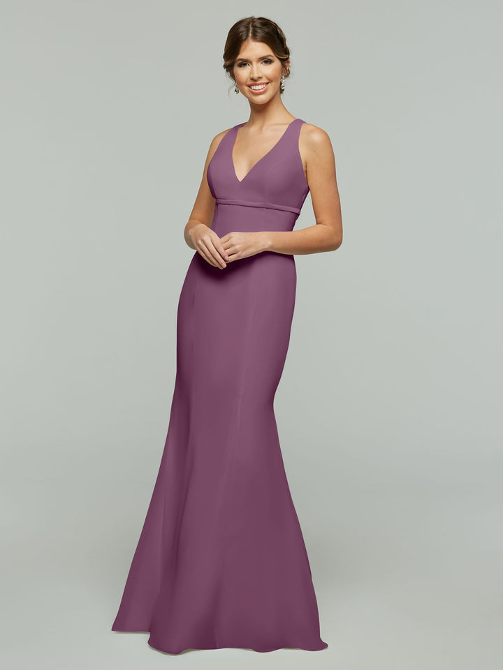 A woman smiles in the Avery Austin 80155, a sleeveless floor-length mauve chiffon dress with a V-neckline and keyhole back. Her hair is in a loose updo as she poses against a plain light gray background.