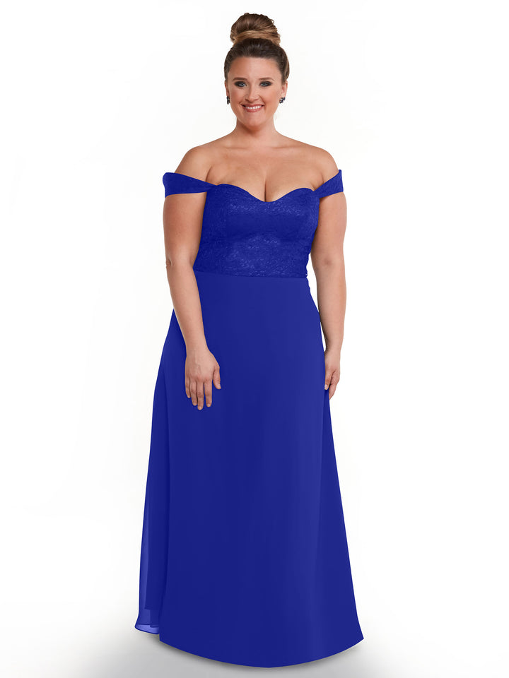 A woman with her hair in a bun is modeling Avery Austin’s 80164, an off-the-shoulder dress with a fitted lace bodice and flowing chiffon skirt, as she smiles against a plain white background.