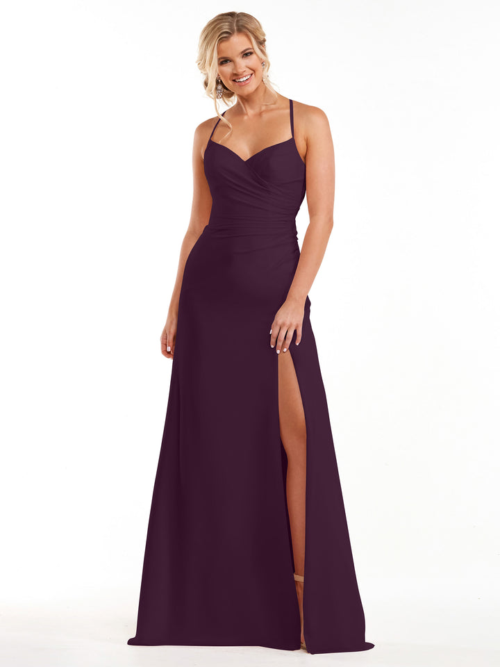 A woman stands smiling against a plain white background, wearing the Avery Austin 80167 bridesmaid dress in Aubergine—a sleeveless, floor-length chiffon gown with thin straps, a sweetheart neckline, ruching, and a high side slit.