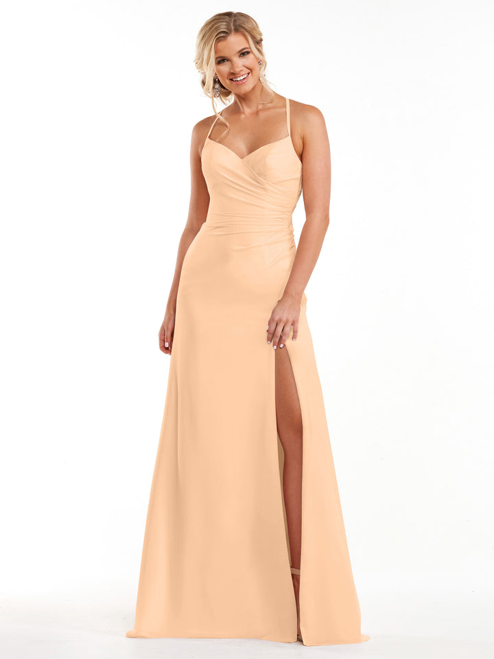 A woman wearing the Avery Austin 80167 blush floor-length ruched chiffon bridesmaid dress with thin straps, a sweetheart neckline, and a high slit stands smiling against a plain white background.