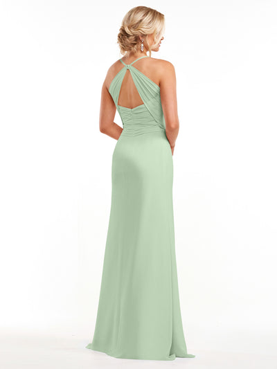 A woman with blonde hair in a low updo and drop earrings wears Avery Austin style 80167, a long light green chiffon gown with gathered fabric and keyhole back, standing with her back to the camera.