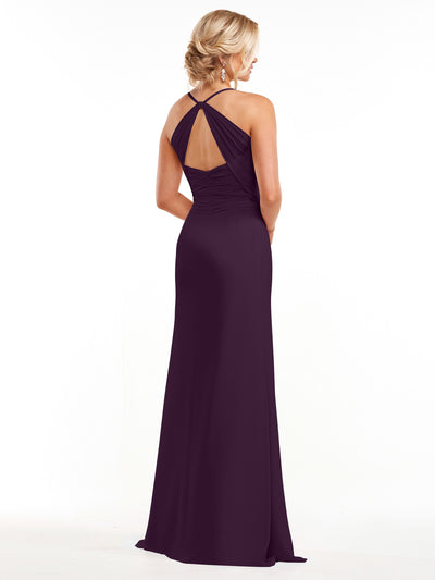 A woman with an elegant low updo stands facing away against a white backdrop, modeling Avery Austin style 80167—a long, sleeveless dark purple chiffon dress with an open back and crisscross halter neckline.