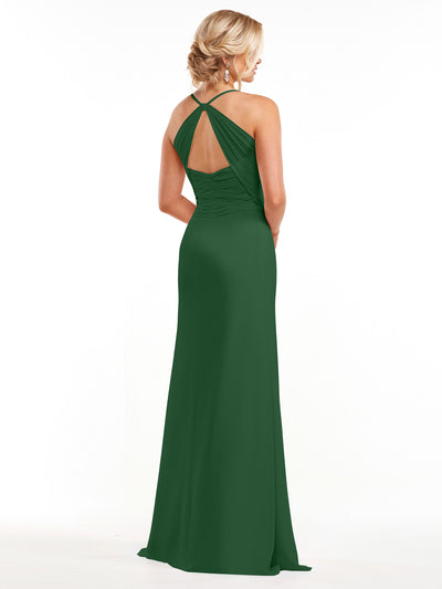 A woman faces away, wearing Avery Austin's 80167—a floor-length dark green chiffon gown with a halter neck, sleeveless design, open crisscross back, and her light hair in an updo. She accessorizes with dangling earrings.