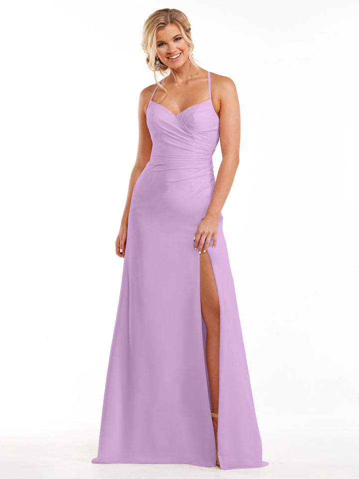 A woman in Avery Austin’s lilac chiffon dress (style 80167) with spaghetti straps and a thigh-high slit stands smiling against a plain white background.