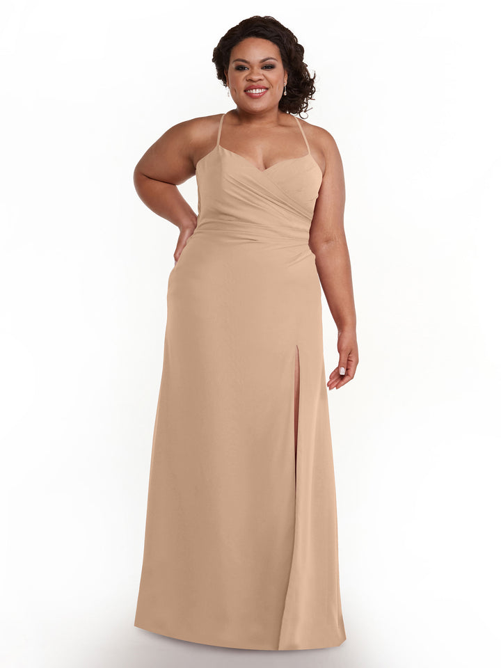 A woman in the Avery Austin 80167 bridesmaid dress in Buff, featuring sleeveless chiffon with thin straps, ruched details, a floor-length skirt with thigh-high slit and sweetheart neckline, smiles against a white background with one hand on her hip.