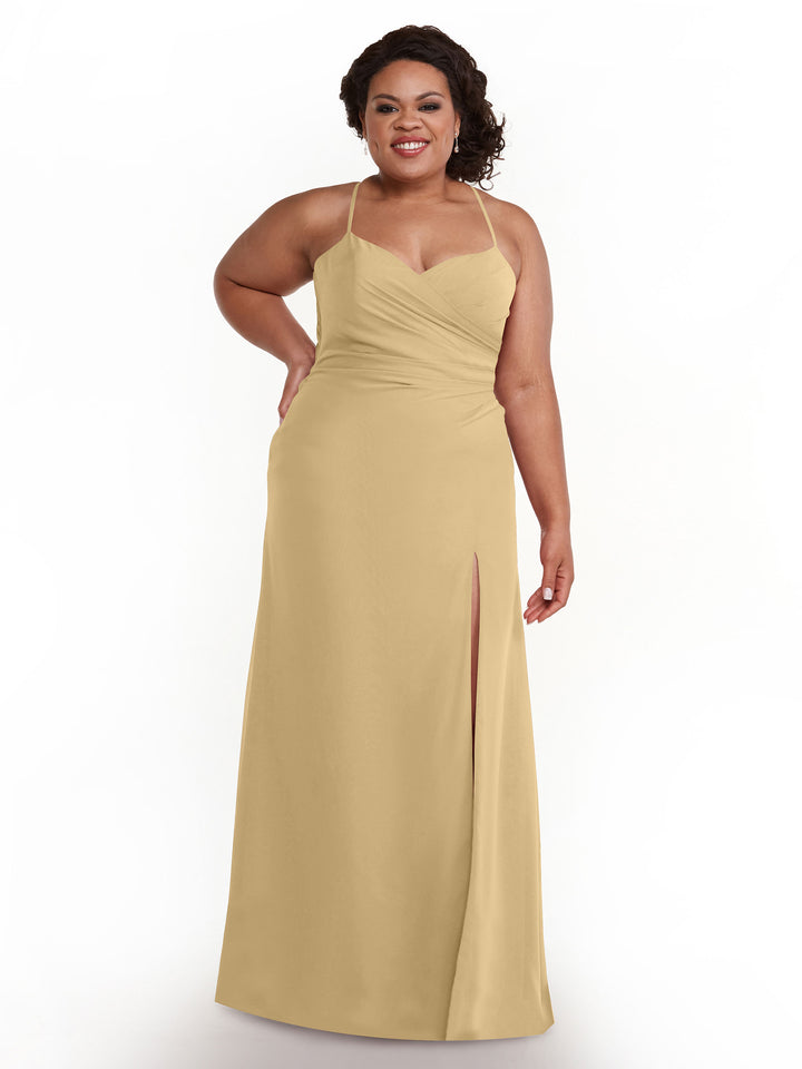 A woman stands smiling against a plain white background in Avery Austin style 80167, a champagne floor-length ruched chiffon bridesmaid dress featuring thin straps, a sweetheart neckline, and a thigh-high slit.