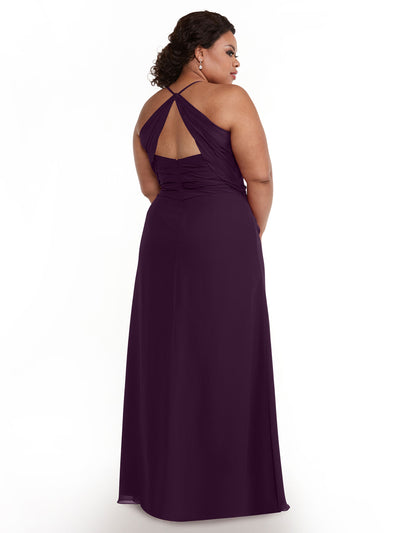 A woman faces away, modeling Avery Austin’s floor-length chiffon dress (style 80167) in deep purple, featuring a crisscrossed open back and delicate spaghetti straps. She poses with softly waved hair against a plain white backdrop.