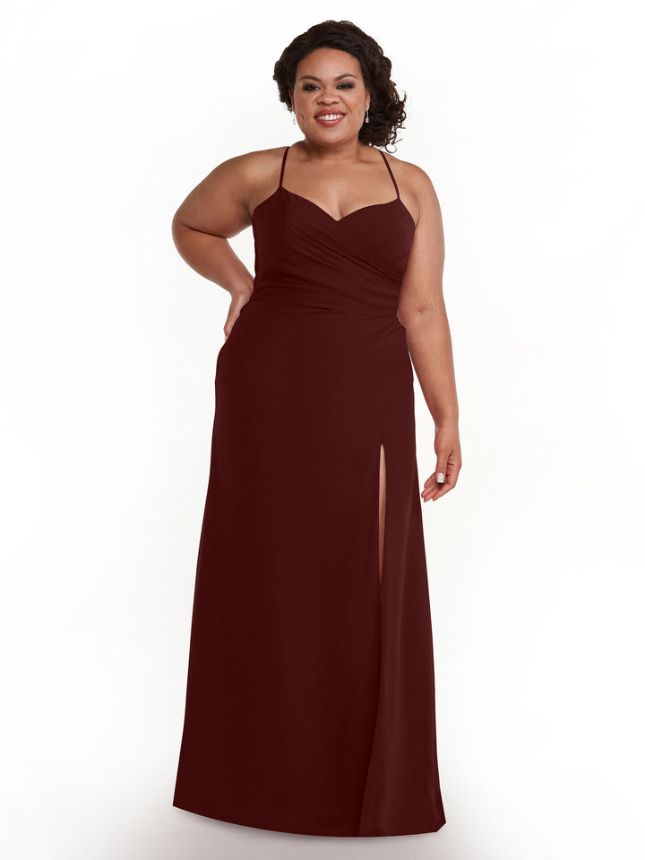 A woman stands smiling against a plain white background, wearing Avery Austin style 80167—a sleeveless Merlot chiffon bridesmaid dress with spaghetti straps, ruching, and a thigh-high slit.