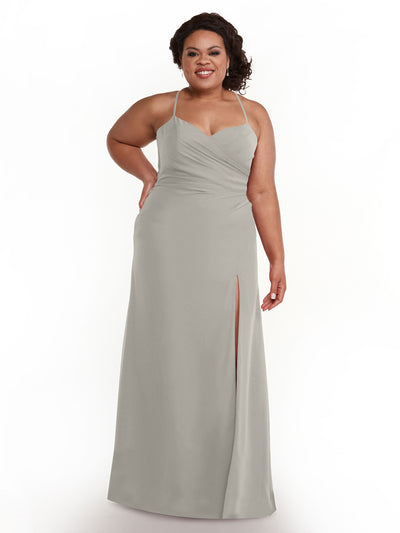 A woman with curly hair wears Avery Austin’s silver floor-length chiffon dress (style 80167) with spaghetti straps, a V-neckline, and a high slit, standing and smiling against a white background.