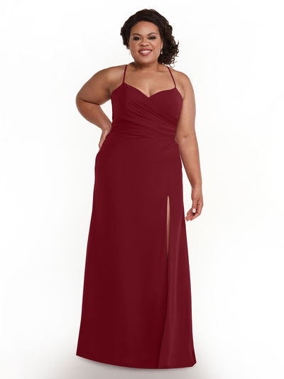 A woman in Avery Austin’s 80167, a floor-length burgundy ruched chiffon bridesmaid dress with a sweetheart neckline and thigh-high slit, stands against a white background, smiling with one hand on her hip.