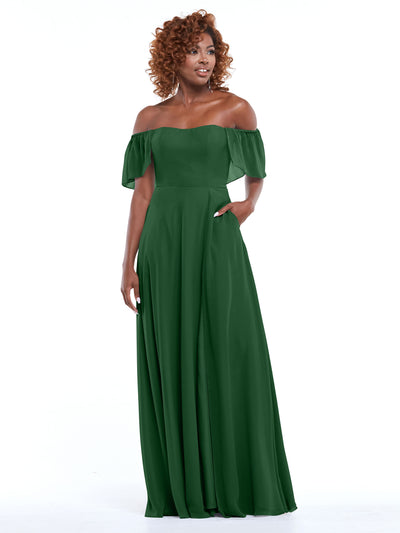 A woman with curly hair models Avery Austin’s 80168, a dark green chiffon off-the-shoulder A-line gown with short ruffled sleeves and pockets, standing against a plain white background.