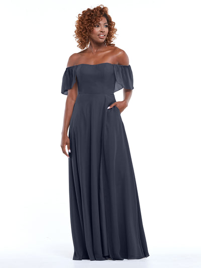 A woman with curly hair models the Avery Austin 80168, a dark gray chiffon A-line off-the-shoulder dress with flutter sleeves and side pockets, against a plain white background.